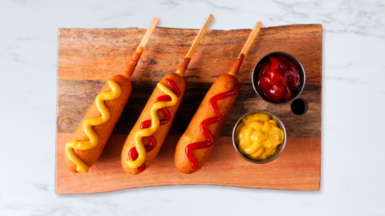 Plate of three corn dogs with ketchup and mustard