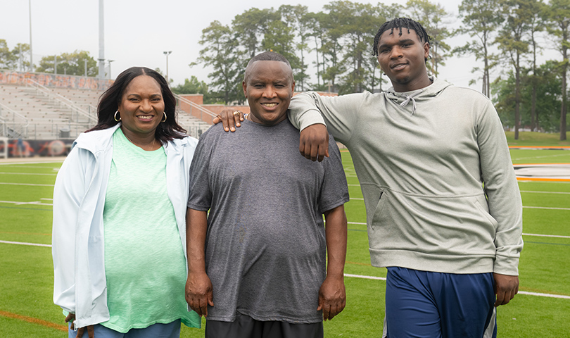 Patrice, Calvin, and their son, Cam, standing together on a football field